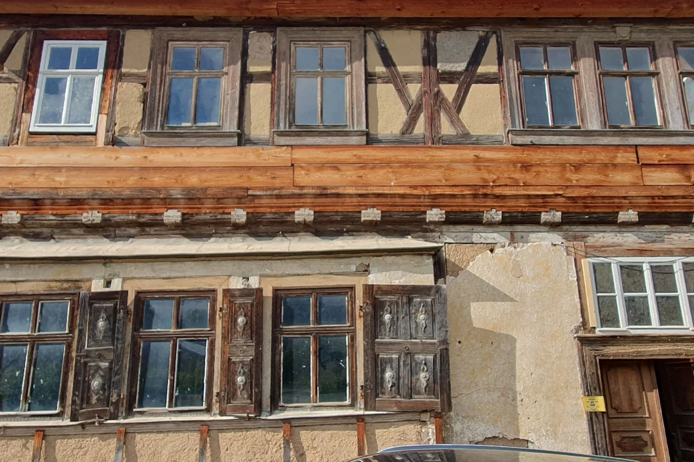 Fassadenausschnitt über zwei Geschosse, oben verputzte Gefache mit Andreaskreuz, unten originale Holzfenster und Fensterläden